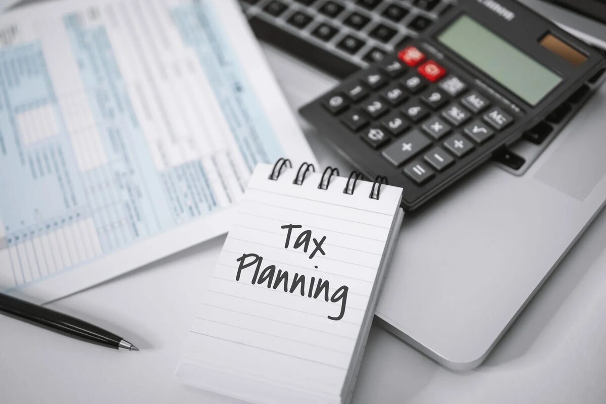 A notepad reading 'Tax Planning' beside a calculator and tax return paperwork on a desk